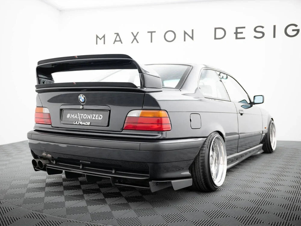 Grey BMW E36 coupe with a large rear wing, aftermarket body kit and deep-dish alloy wheels.